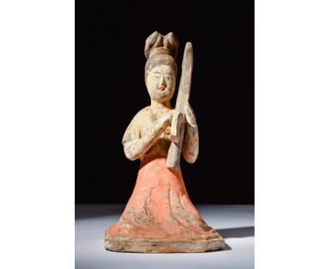 Ca. AD 618 - 907.A terracotta figure of a seated female harpist. The woman is shown kneeling with her legs tucked beneath a w