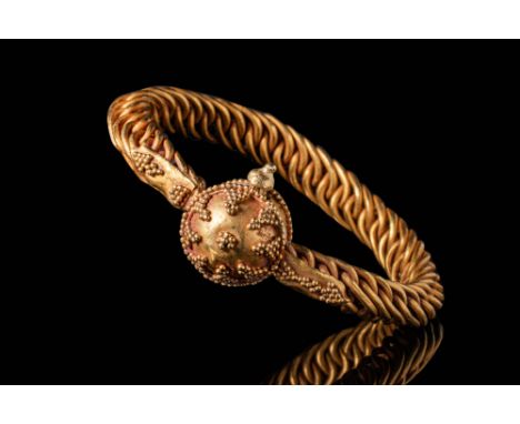 Ca. AD 1100. A solid gold bracelet with a densely braided wire band forming a continuous loop. At the centre, a dome-shaped b