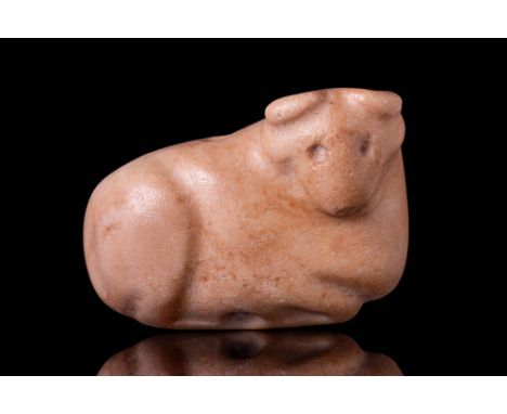Ca. 3000 BC. A stylised bull amulet carved from stone, shown reclining with legs tucked beneath and head turned. The back is 