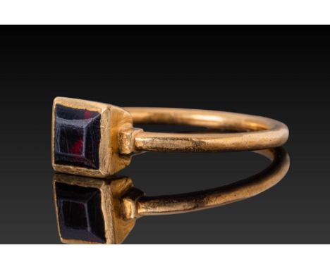 Ca. AD 1300 - 1600. A gold ring with a slender circular hoop and a sharply angled square bezel set with a faceted red garnet.