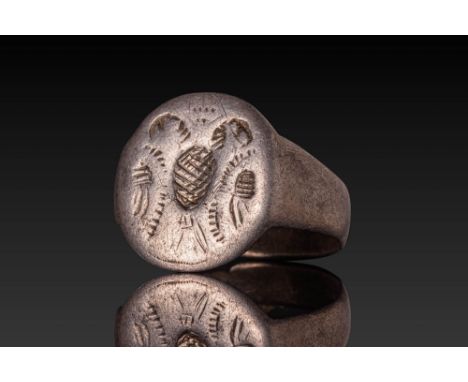 Ca. AD 1000 - 1100. A silver ring with a broad, flat hoop that tapers slightly towards the back. The circular bezel is engrav