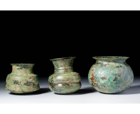 Ca. 1100 - 800 BC. A collection of three bronze vessels. The one on the left has a flaring body and a neck with a slightly ev