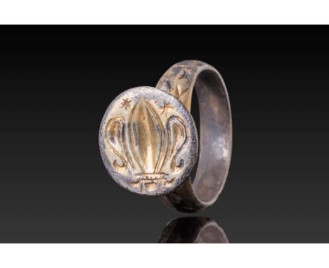 Ca. AD 1200 - 1500. A silver-gilt ring with a slightly recessed circular bezel engraved with a stylised fleur-de-lis flanked 