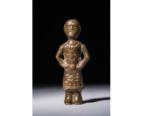 Ca. AD 800 - 1100. A bronze female figure standing in a rigid frontal pose with hands placed on the waist. The head is rounde