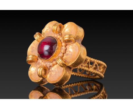 Ca. AD 500 - 700. A gold ring with a flower-shaped bezel set with a central garnet cabochon framed by a border of granules. T