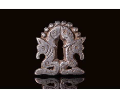 Ca. AD 800 - 1000. A silver appliqué of compact, arched form with a vertical slot at the centre. The front face displays a sy