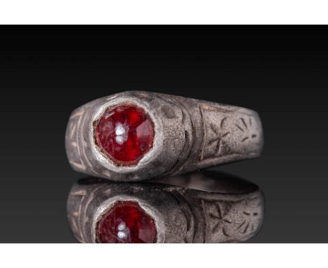 Ca. AD 1200 - 1400. A silver ring with a rounded hoop that widens gently to support a tall, conical bezel set with a deep red
