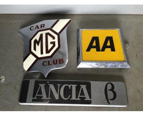 An MG Car Club part enamel car badge, a Lancia B insignia badge and an AA badge.
