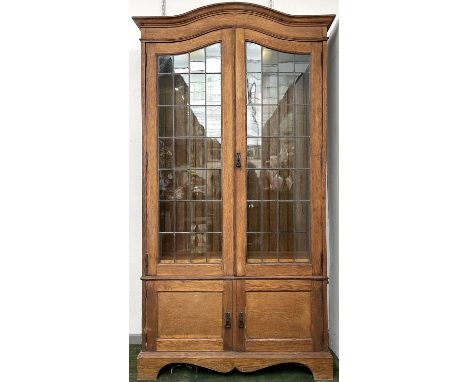 An oak bookcase, early 20th century, in the Arts and Crafts taste, with arched top and leaded glazed doors enclosing adjustab