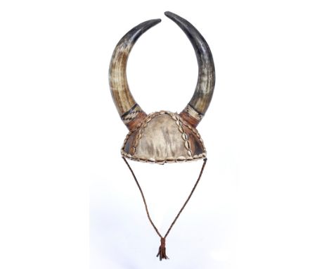 A NIGERIAN ANIMAL SKIN AND SHELL MOUNTED HELMET with double horns, 40cm high -  Purchased Sothebys 1969