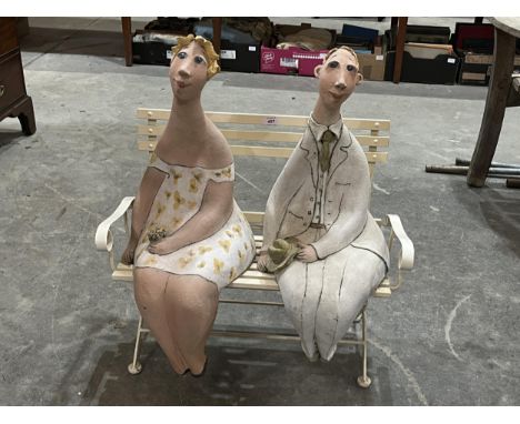 A metal slatted bench, 26" wide; together with a pair of seated ceramic figures.