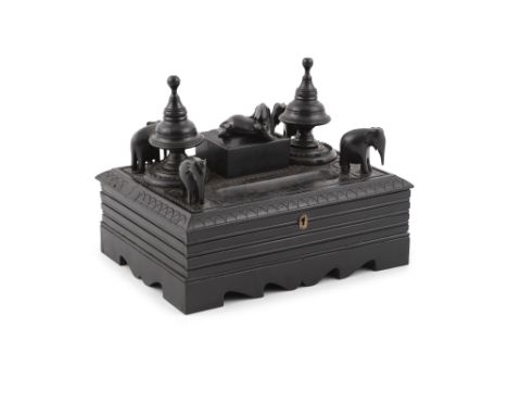 A 19TH CENTURY ANGLO INDIAN EBON STANDISH, of rectangular form, carved with elephants in relief, centred with a compartment b