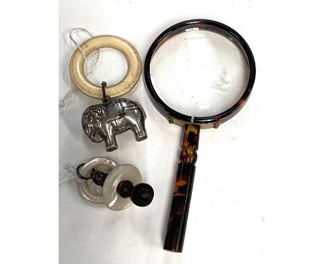 A vintage tortoise shell effect magnifying glass, a silver and mother of pearl rattle/ teething ring and another plated eleph