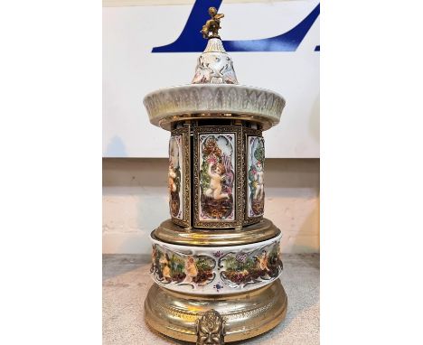 A ceramic and gilt cigarette/lipstick dispenser with Swiss musical movement, ceramic panel decorations in relief playing the 