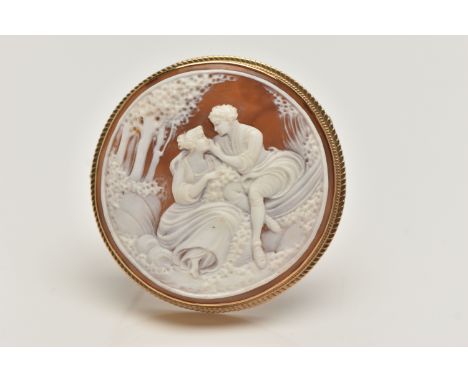 A 9CT GOLD CAMEO BROOCH, of a circular form, carved shell cameo depicting a couple scene, collet set with a fine rope twist s