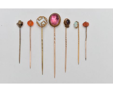 SEVEN YELLOW METAL STICK PINS, to include a pink foiled back paste cabochon in a yellow metal and black enamel mount, unmarke