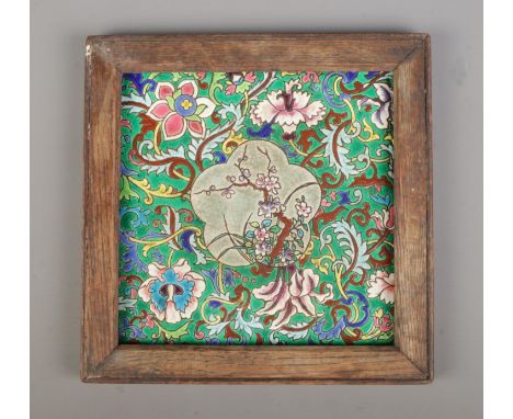 A Longwy style ceramic tile with enamelled foliate decoration. In wooden frame. Tile size 20cm x 20cm.