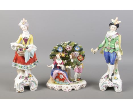 Three antique ceramic figures, consisting of man and woman fruit pickers, on similar scrolled bases topped with flowers and p