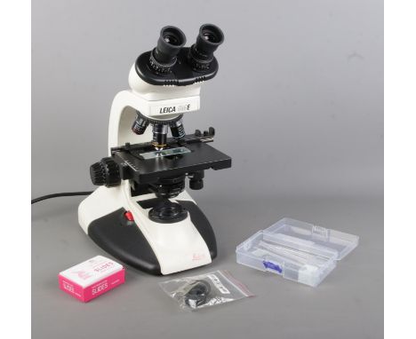 A Leica CM E binocular microscope, featuring 4X, 10X, 40X, 100X lenses. With branded protective dust jacket and accessories i