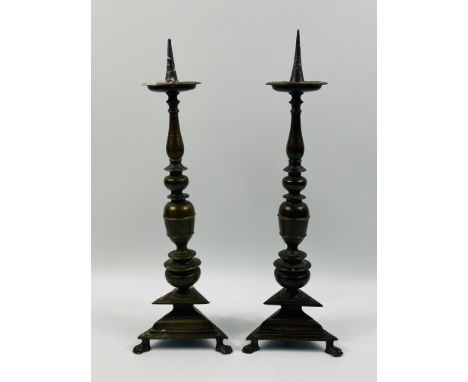 A pair of 19th century Continental heavy bronze pricket candlesticks with a decorative central column and raised upon a stepp