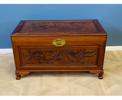 A Chinese carved hardwood blanket chest with carved decoration to the front and top with the sides panelled, central brass lo