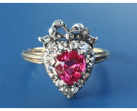 An Edwardian synthetic ruby &amp; diamond set heart-shaped cluster ring, surmounted by a tied ribbon, on a yellow metal shank