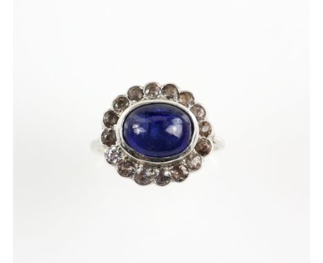 Art Deco period ring set with a central blue cabochon sapphire, within a border of white sapphires, set in unmarked white met
