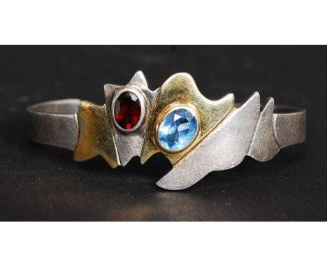 A contemporary ladies silver and gilded silver 925 marked bangle with inset ruby garnet stone and cornflower blue stone. Tota