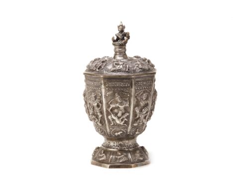 A LARGE BURMESE SILVER VASE AND COVER
Octagonal, decorated with figures in relief set into panels in three rows, the finial i