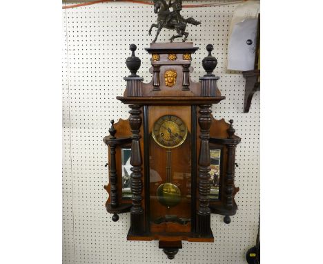 AN UNUSUAL VIENNA TYPE WALL CLOCK, pendulum driven brass faced movement in a walnut and mixed wood case, having turned and fi