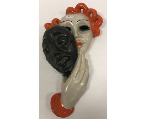 A Goldscheider glazed terracotta wall mask as a young woman holding a theatrical face mask, No'd verso "6288-130-65" 35.5 cm 