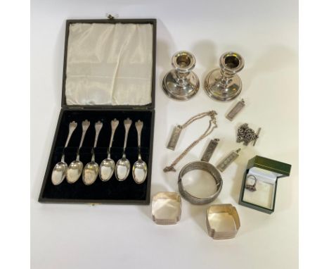 A collection of assorted silverware including a pair of weighted dwarf candlesticks; four ingot pendants; a pair of serviette