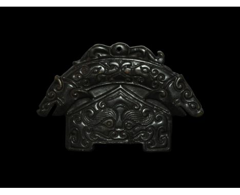 19th-20th century AD. A black jade plaque formed as a central section with triangular upper part, with facing mask and swirls