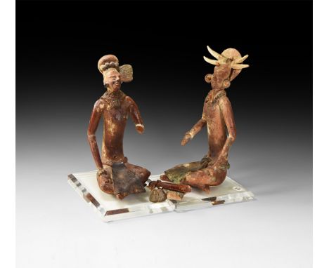 A pair of undated archaistic ceramic figures, each a seated male in loincloth with crossed legs, one hand resting on a knee a