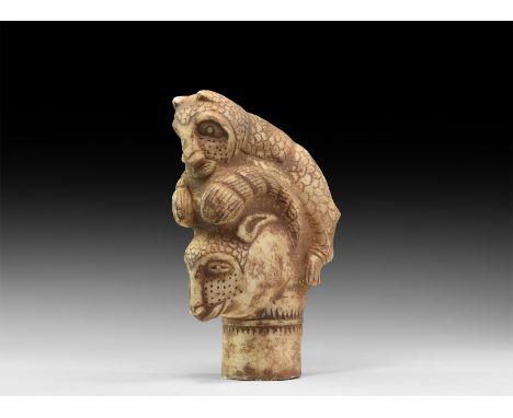 An undated archaistic carved stone finial formed as a feline pouncing on a ram(?), on a columnar base.  3 kg, 24cm (9 1/2"). 