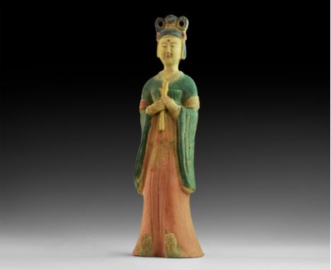 20th century AD. A hollow-formed ceramic statuette of a robed lady with elaborate hairstyle, hands clasped to the chest holdi
