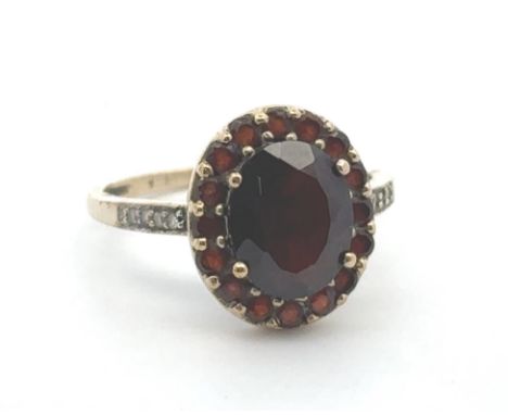 A red and white stone cluster ring, stamped 9k. Oval dark red paste centre stone surrounded by smaller red stones likely past