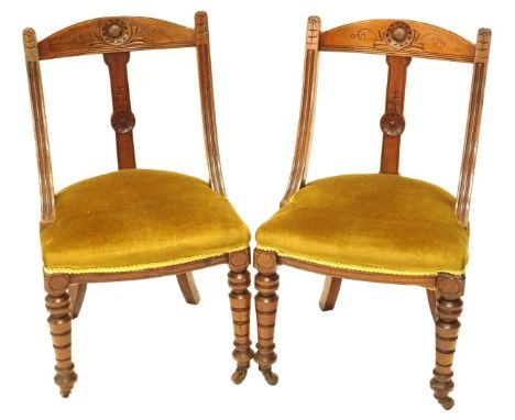 A pair of Victorian spoon back type chairs, each carved with flowerheads, with a padded seat on cabriole legs with ceramic ca