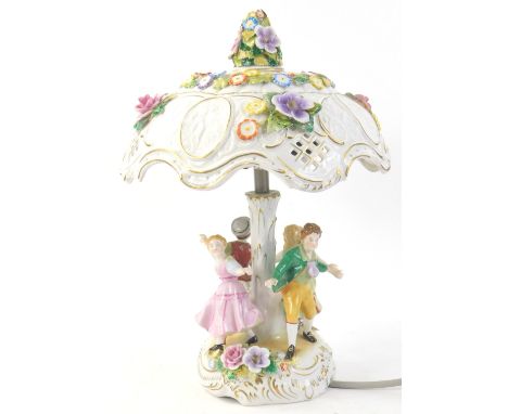 A German porcelain lamp base, with lithophane and floral encrusted shade, the base applied with four dancing figures, printed