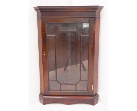 A Georgian-style (later) mahogany corner cupboard: dentil cornice and single glazed door enclosing shelf and raised on shaped