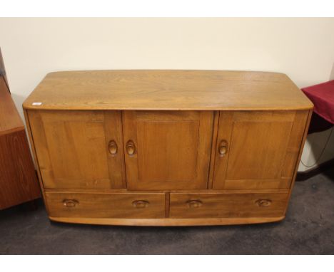 An Ercol sideboard enclosed by three doors above two base drawers, raised on castors, 130cm wide x 50cm deep