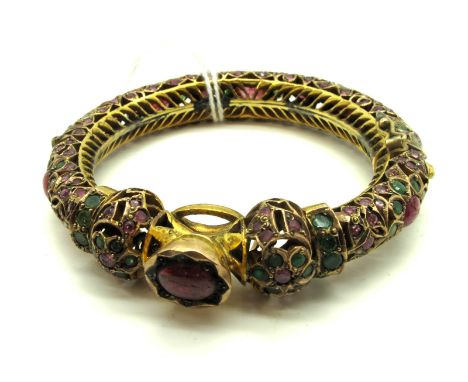 A Multi Gem Set Bangle, of Middle Eastern style with ruby cabochon highlights, hinged to snap clasp, stamped "14KT". 