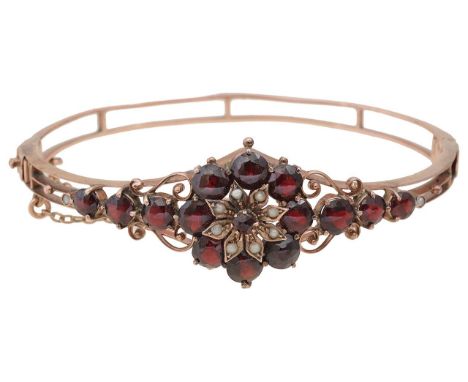 A garnet open-work banglecentral floral cluster set with seed pearls, within domed faceted garnet surround, with scrolling wi
