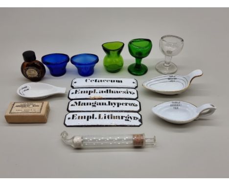 A small group of apothecary and pharmacy items,&nbsp;to include: glass eye baths; and four enamel labels, 12cm wide. 