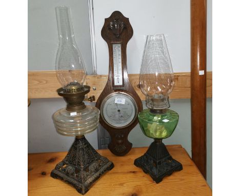 Two Victorian cast iron and glass oil lamps; an aneroid barometer with thermometer 