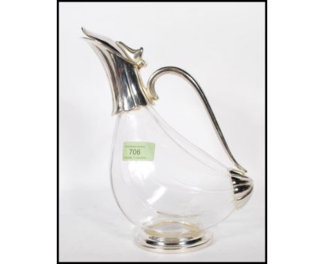 A 20th Century glass wine decanter of tilted form having silver white metal fixtures, being raised on a round base with a scr