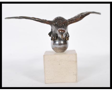 A vintage 20th Century car mascot in the form of a vulture with spread wings mounted on an orb above a chamfered square stone