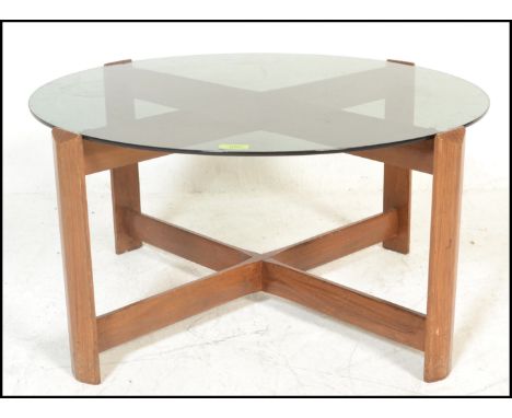 A mid century retro teak wood and smoked glass circular coffee - occasional table. Raised on shaped supports united by cross 