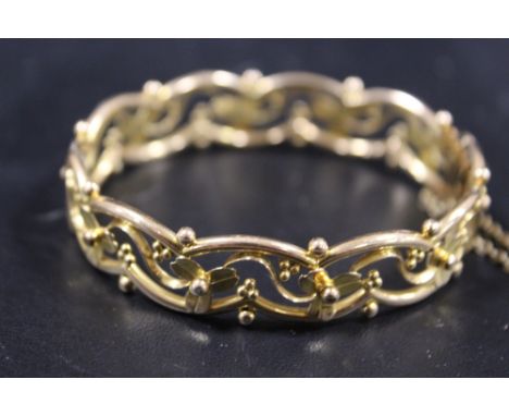 AN ORNATE CONTINENTAL YELLOW METAL BANGLE STAMPED 15 WITH DECORATIVE FLORAL WIREWORK DESIGN AND SAFETY CHAIN TO CATCH - APPRO