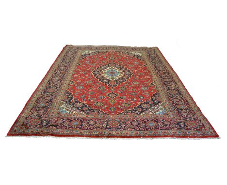A Kashan carpet, cream and blue geometric pole lozenge, surrounded by stylised flowers on a red ground framed by spandrels an